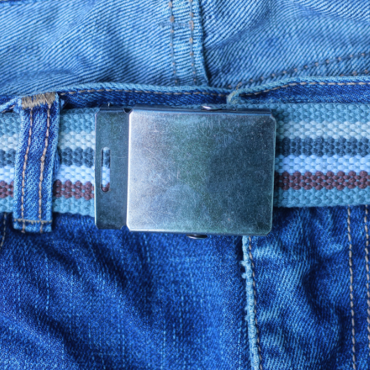 Ceinture en tissu rayée avec boucle métallique fixée à un jean en denim bleu.