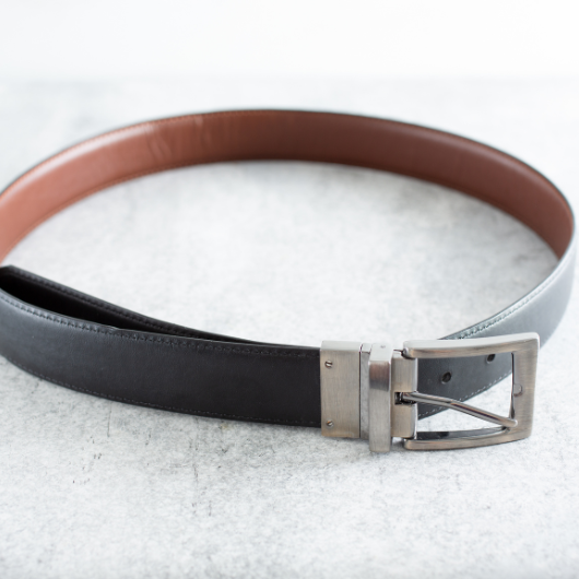 Ceinture réversible noire et marron pour homme avec boucle en métal, posée en cercle sur un fond clair.