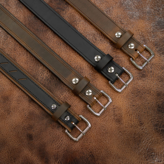 Ensemble de ceintures réversibles pour homme en cuir noir et marron, alignées sur un fond en cuir.