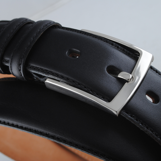 Gros plan sur une ceinture réversible en cuir noir avec boucle argentée brillante.
